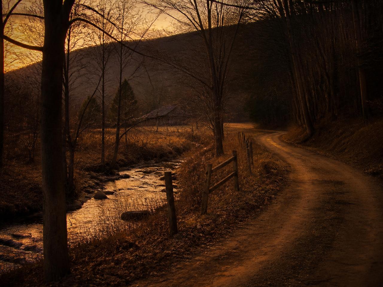 A dirt road winding past a creek and an old barn at dusk in rural Pennsylvania
